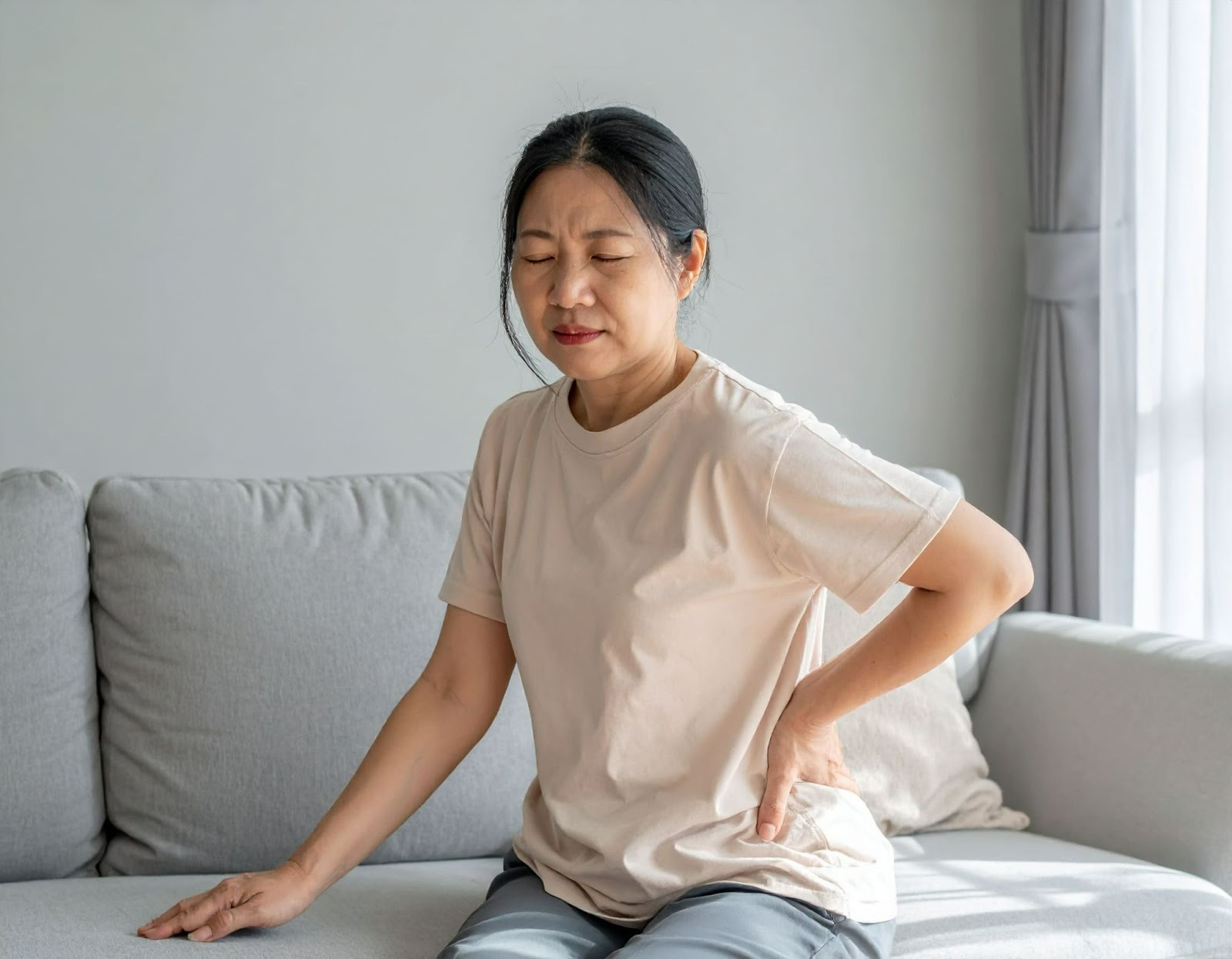 女子腰痛坐在沙發上扶著下背