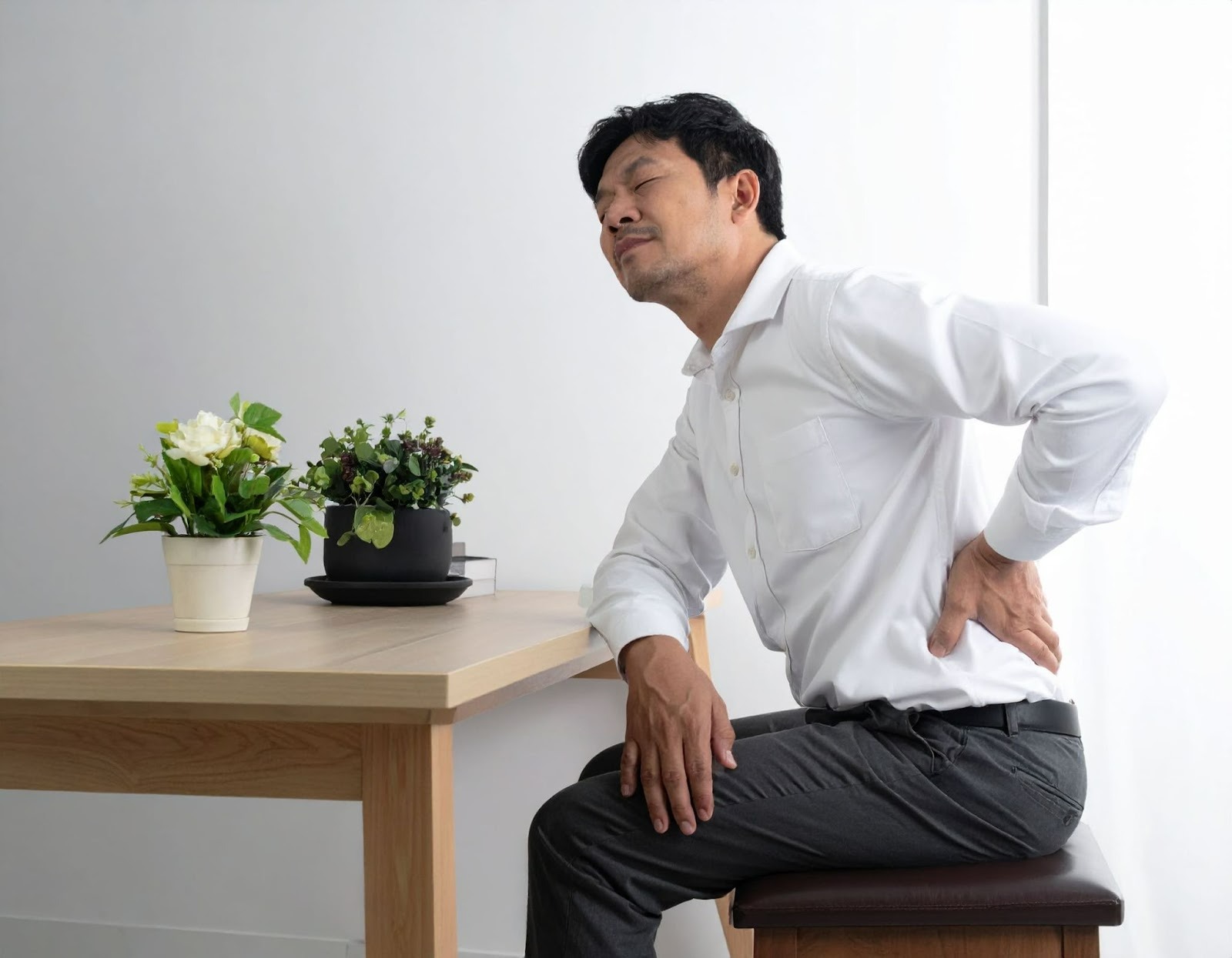 男子坐在椅子上按摩背部，露出腰部不適表情